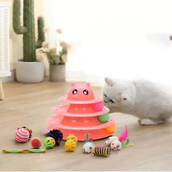 Jeux Chat - Feline Turbo Tower, Phase 3 Rose suscitant la curiosité d'un chaton blanc, entourée d'accessoires variés sur le sol