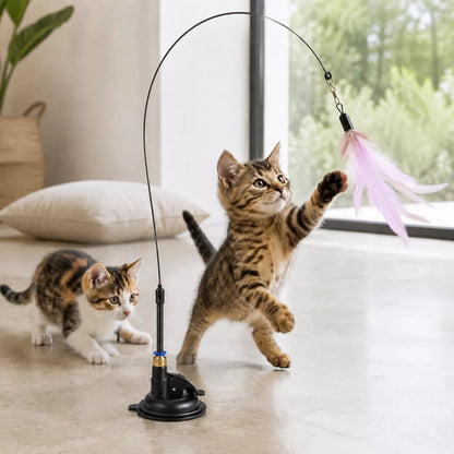 Plume pour chat AéroPlume Féline à ventouse, attrapée par un chaton tigré sous le regard d’un chaton isabelle près d’une baie vitrée